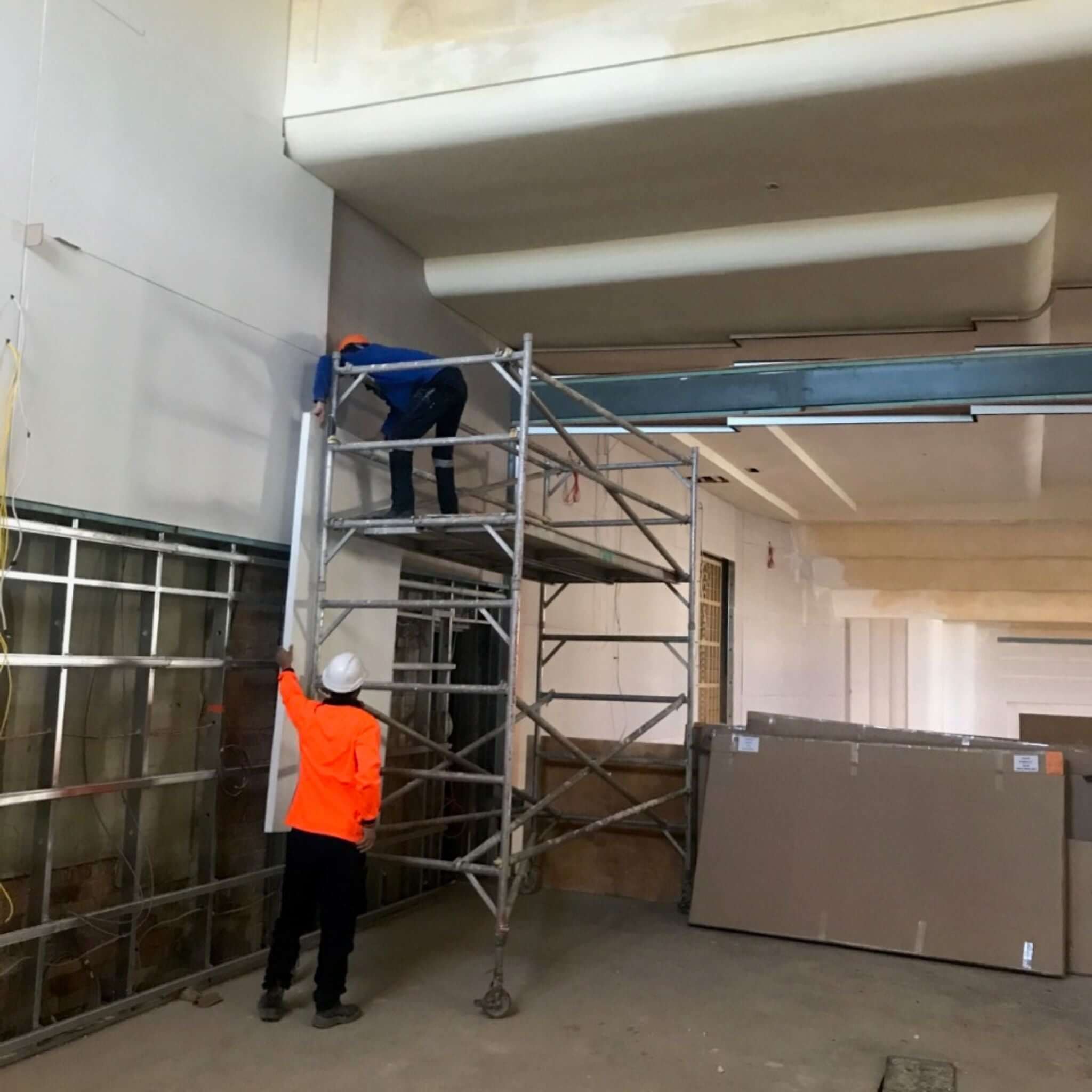 Two construction workers on a scaffold performing interior work in a building under renovation.