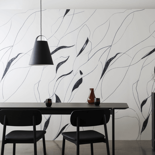 Elegant dining area featuring a black and white leaf-patterned wall, minimalist furniture, and a modern pendant light.