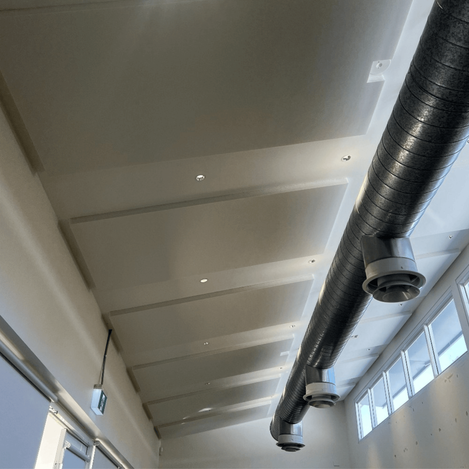 Autex Quietspace® ceiling panels installed in St Ives Youth Hub, viewed from corner with ductwork and downlights