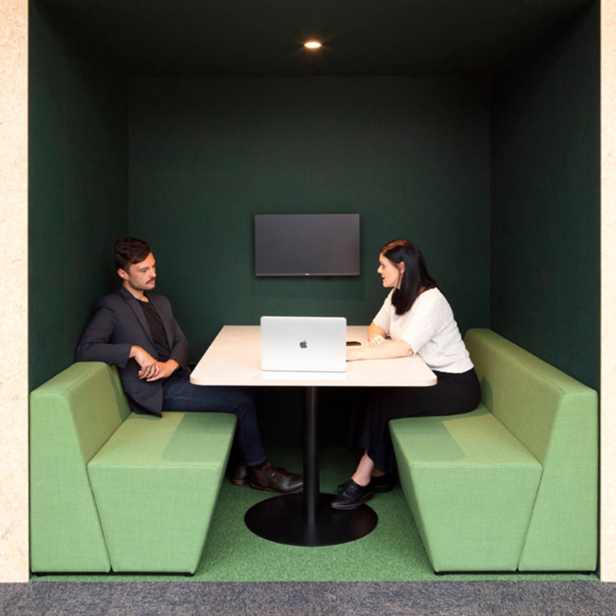 modern workspace featuring two professionals discussing in a soundproof meeting booth with green acoustic panels.