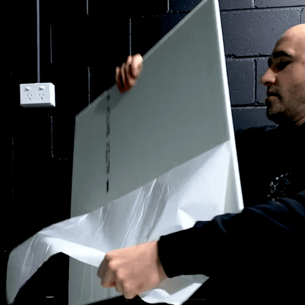 Man peeling the backing from Autex Composition® acoustic tile for installation against a dark wall.