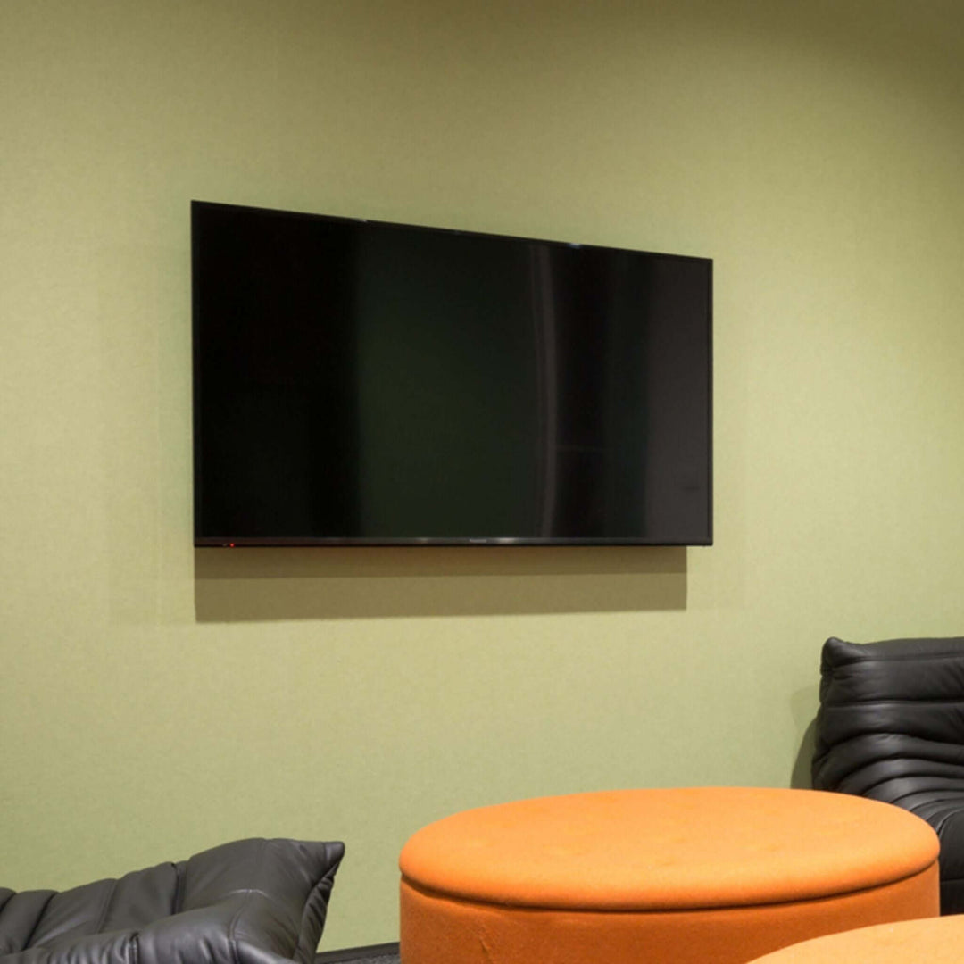 Modern lounge area featuring a mounted TV on a green wall with orange circular table and black seating.