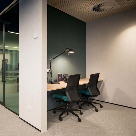 Modern office workspace with two ergonomic chairs, a desk, and soft lighting, featuring an acoustic wall cover.