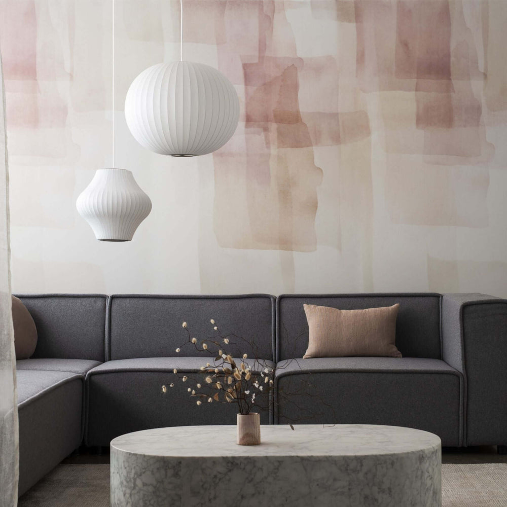 Modern living room with gray sofa, marble coffee table, and stylish pendant lights against a soft pink abstract wall.