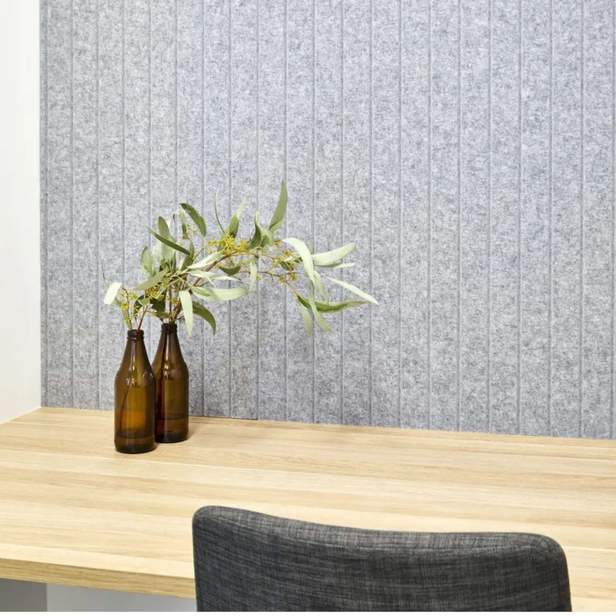 Autex Groove Acoustic Panels on a decorative wall with brown bottles and greenery on a wooden desk.