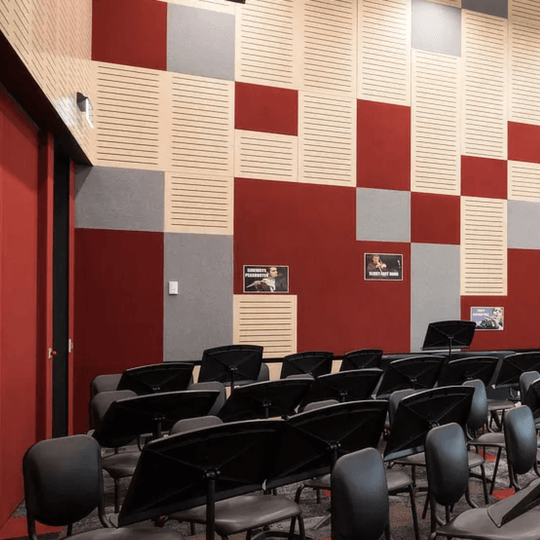 Colorful acoustic wall design featuring red, gray, and beige tiles in a music room with black chairs and posters.