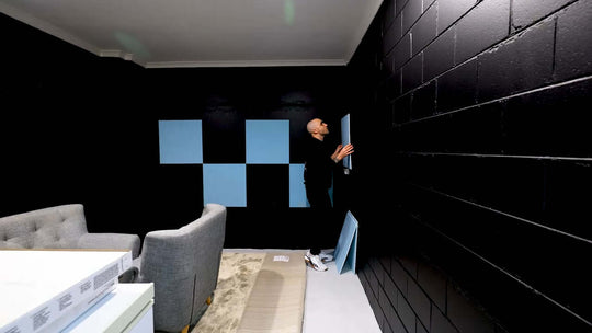 person applying Autex Peel n Stick Acoustic Tiles on a black wall in a modern living space, showcasing DIY acoustic solutions.