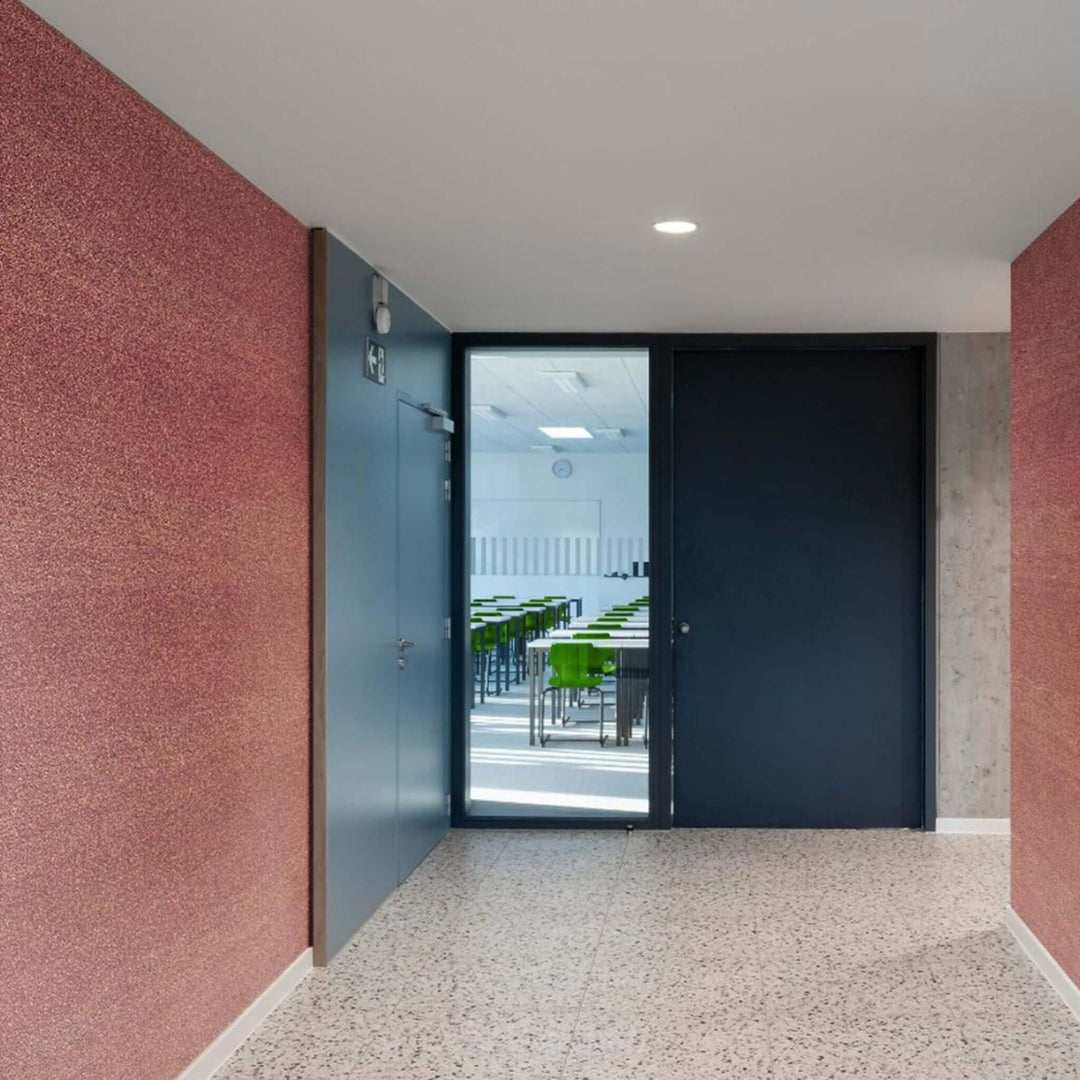 Modern hallway with textured red walls leading to a classroom with green chairs and natural light.