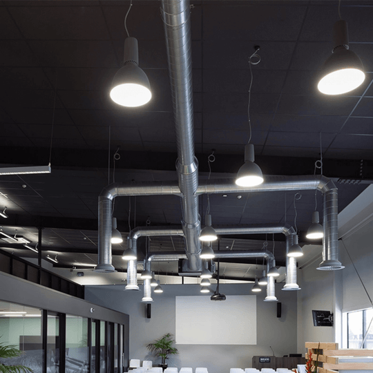 Modern office interior featuring industrial lighting and exposed ductwork on a black ceiling.