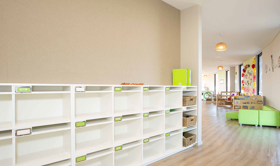 Bright and spacious childcare centre with white storage shelves, natural wood flooring, and colourful decor.