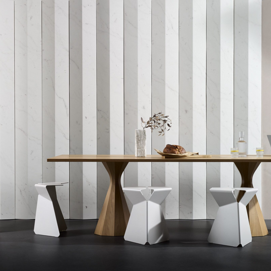 Modern dining space featuring a wooden table and unique white stools against a striped marble wall design.