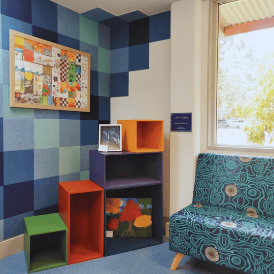 Colorful wall with acoustic tiles, vibrant shelving units, and patterned seating in a bright interior space.