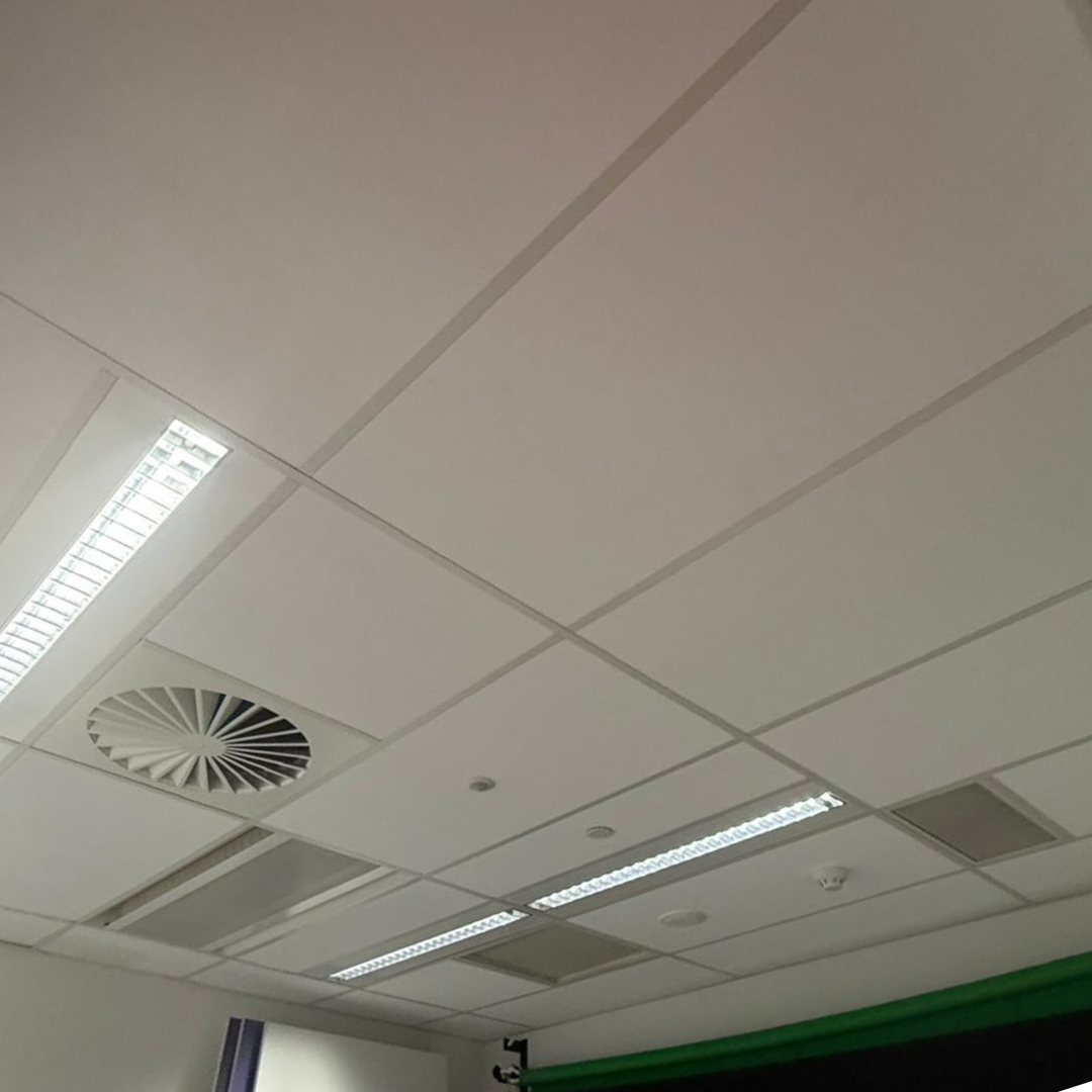 White acoustic ceiling tiles with integrated fluorescent light strips and a circular ventilation grille in a drop-tile office ceiling.