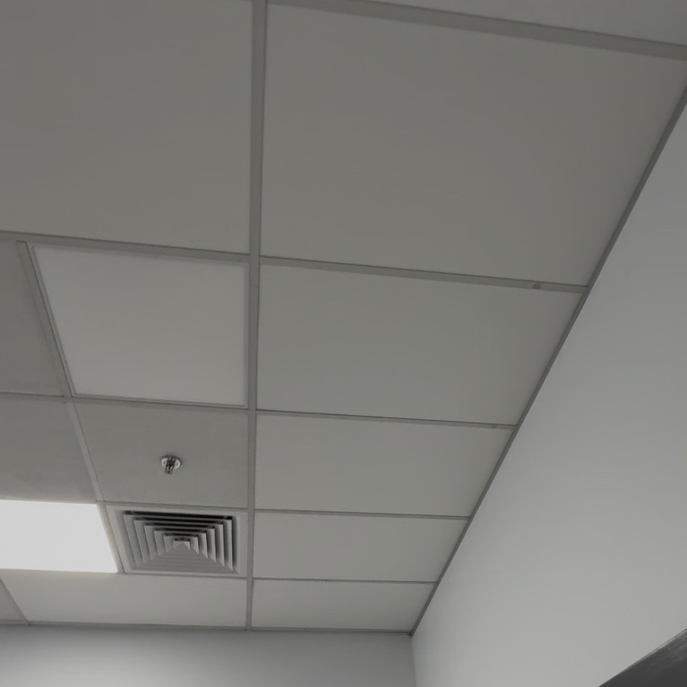 White ceiling tile grid with a square fluorescent light and a metal ventilation grille in one panel.
