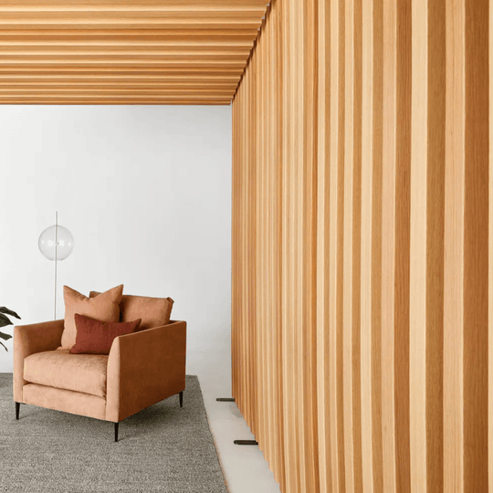 Modern living space featuring Autex Acoustic Timber Rafts and a stylish brown armchair against a wooden slatted wall.